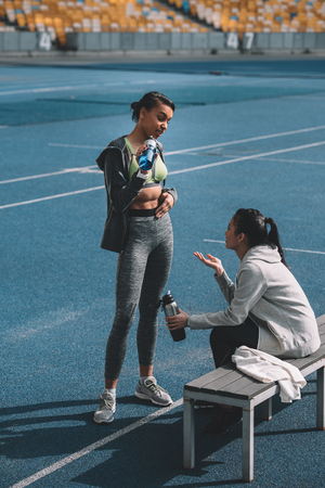 Athletic young women in sportswear drinking water from sports bottles on stadiumの写真素材