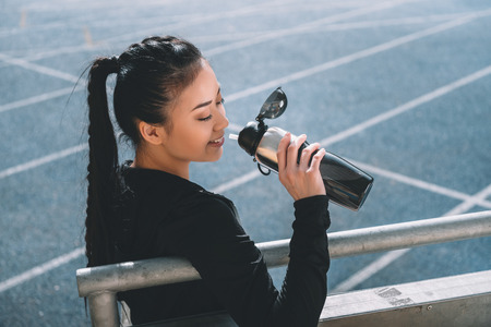 sportswoman drinking water on running track on stadiumの写真素材