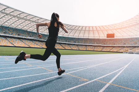 young woman in sportswear sprinting on running track stadium at sunset
