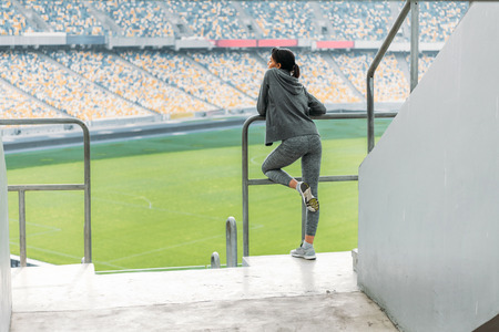 american young sportswoman standing at handrail on stadiumの写真素材