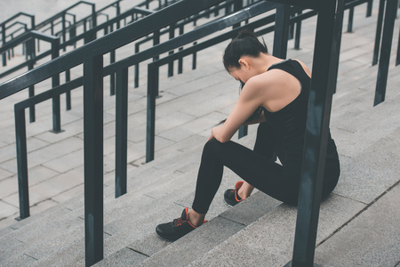 tired sportswoman in sportswear sitting on stadium stairsの写真素材