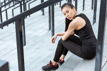 young asian sportswoman sitting on stadium stairs and looking at cameraの写真素材