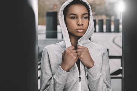 young fitness woman in sportswear wearing hood and posing on stadium