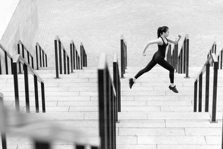Side view of athletic young woman in sportswear running on stadium stairsの写真素材