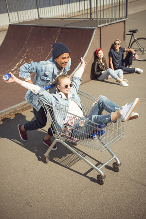 Boy carrying happy girl in shopping cart while friends sitting near rampの写真素材
