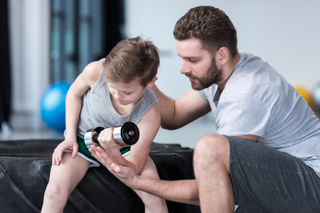Boy training with dumbbell together with coachの写真素材