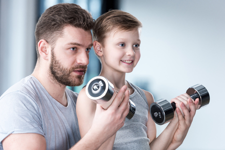 Boy training with dumbbells together with coachの写真素材