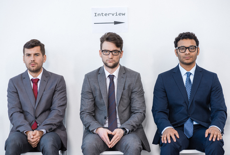 businessmen in suits sitting on chairs at white waiting roomの写真素材