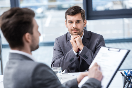 Handsome young businessman looking at manager with clipboard at job interviewの写真素材