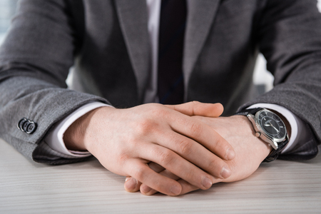 partial view of businessman with hands in lock sitting at tableの写真素材