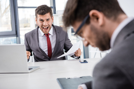 boss with documents shouting at upset colleague at workplaceの写真素材