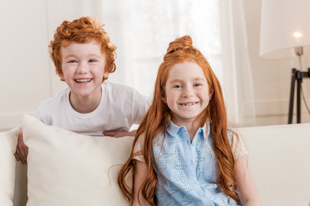 adorable redhead sister and brother sitting together on sofa at homeの写真素材