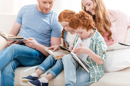 Beautiful redhead family sitting on sofa and reading books togetherの写真素材