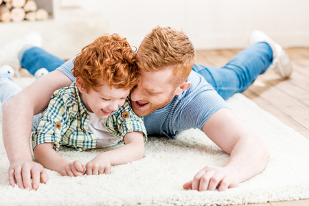 Happy redhead father and son having fun together on carpet at homeの写真素材