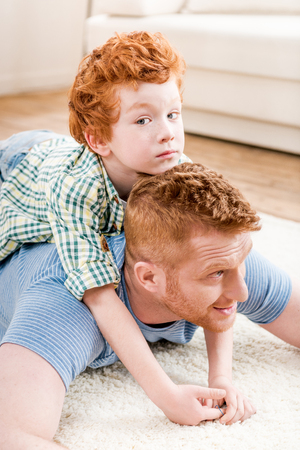 Happy redhead father and son having fun together on carpet at homeの写真素材