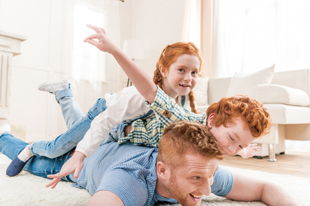 Happy father with adorable redhead children playing and having fun together on floorの写真素材