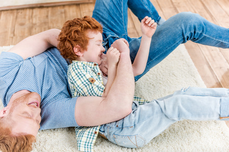 Happy redhead father and son playing together on carpet at homeの写真素材