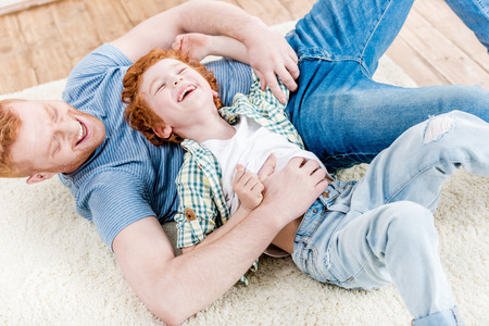 Happy redhead father and son playing together on carpet at homeの写真素材