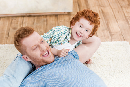 Happy redhead father and son playing together on carpet at homeの写真素材