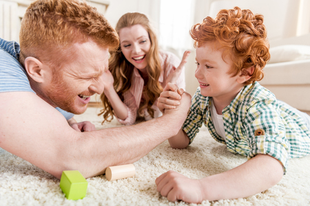 side view of father and son playing arm wrestling with mother near byの写真素材