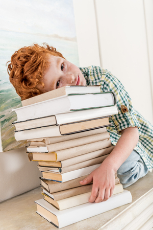 pensive little boy leaning on pile on booksの写真素材