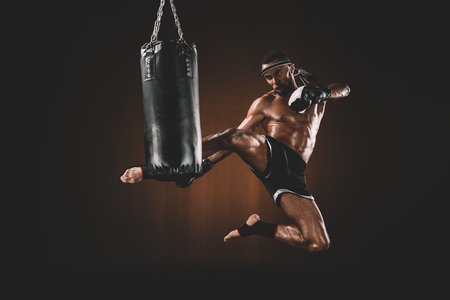 side view of focused muay thai fighter practicing kick on punching bagの写真素材