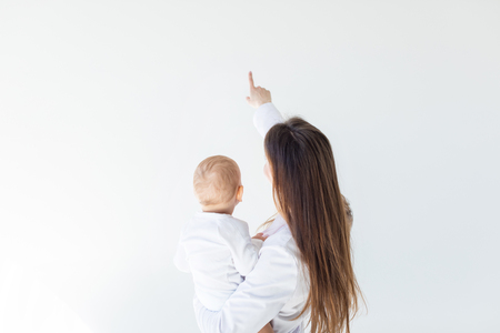 rear view of mother holding adorable baby boy and pointing isolated on white, 1 year old baby conceptの写真素材