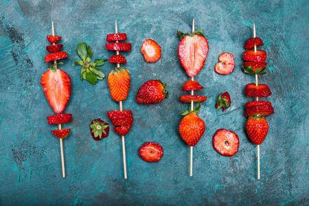 whole fresh red strawberries and sliced strawberries on wooden skewers, berries top view conceptの写真素材