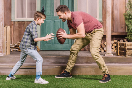 father with little son playing american football with ball at backyardの写真素材