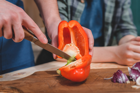 Close-up partial view of father and son cutting pepper on wooden cutting boardの写真素材