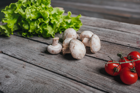 close up of cherry tomatoes with mushrooms and salad on wooden tableの写真素材