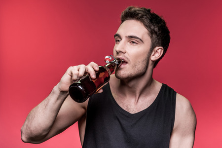 young man in black vest drinking beer and looking away