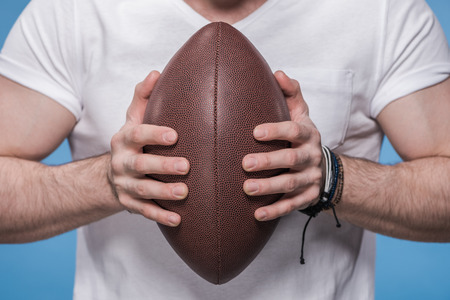 Close-up partial view of young man in white t-shirt holding rugby ballの写真素材