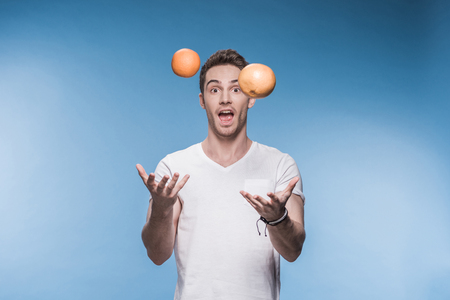 young man juggling with fruits isolated on blueの写真素材