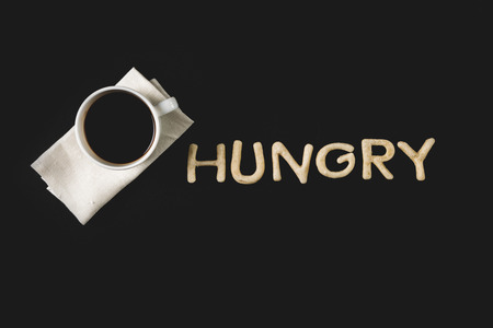 top view of word hungry made from cookie dough and coffee cup isolated on blackの写真素材