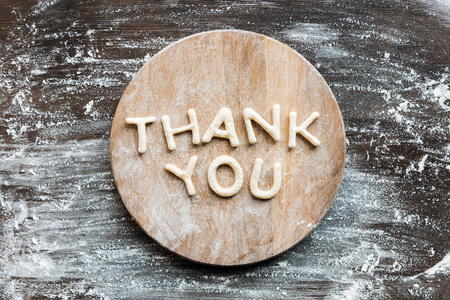 top view of lettering thank you made from cookie dough with flour on wooden cutting boardの写真素材