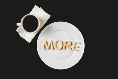 top view of more word  made from cookie dough on plate with coffee cup isolated on blackの写真素材