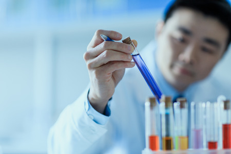 Close-up view of asian scientist in lab coat holding test tube with reagent
