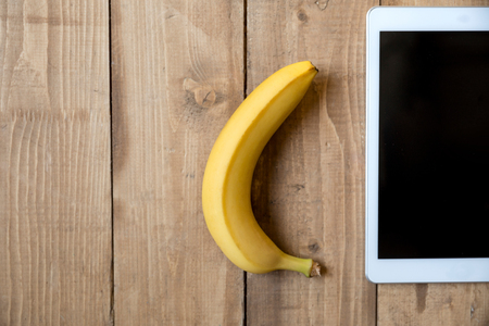 Top view of fresh ripe banana and digital tablet on wooden surfaceの写真素材