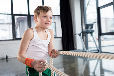 adorable kid boy in sportswear training with ropes at fitness studioの写真素材