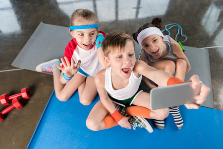 High angle view of cute sporty kids taking selfie with smartphone in gym