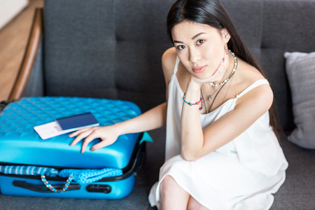 asian woman traveler sitting on sofa with suitcase and passport, packing luggageの写真素材