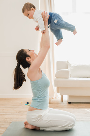 Young mother playing with her son at home in sunny dayの写真素材