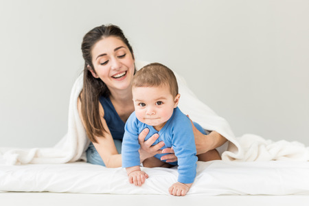 mother with her son playing under white blanket at homeの写真素材