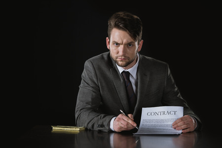 serious businessman pointing on contract isolated on blackの写真素材