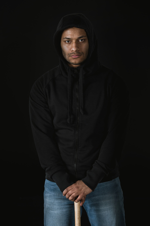 african american robber in zoodie with baseball bat isolated on blackの写真素材