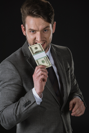 businessman biting dollar banknotes isolated on blackの写真素材