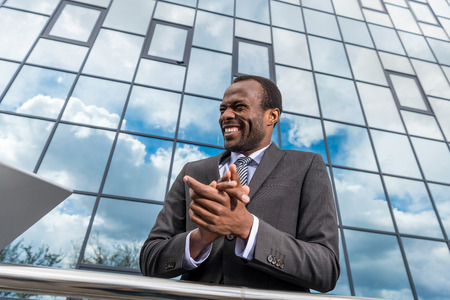 successful african american businessman laughing and gesturing while standing at office buildingの写真素材