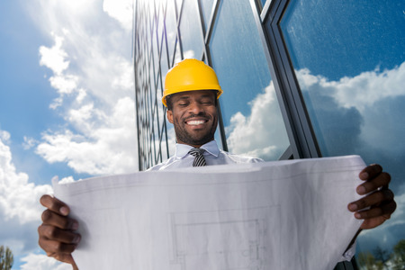 professional architect in hard hat holding blueprint outside modern building
