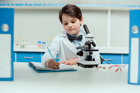 schoolboy with microscope and copybook in science laboratory